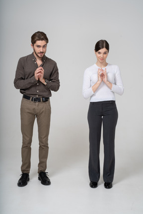 Front view of a sly young couple in office clothing holding hands together