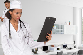 A female doctor holding a clipboard with male doctor on background