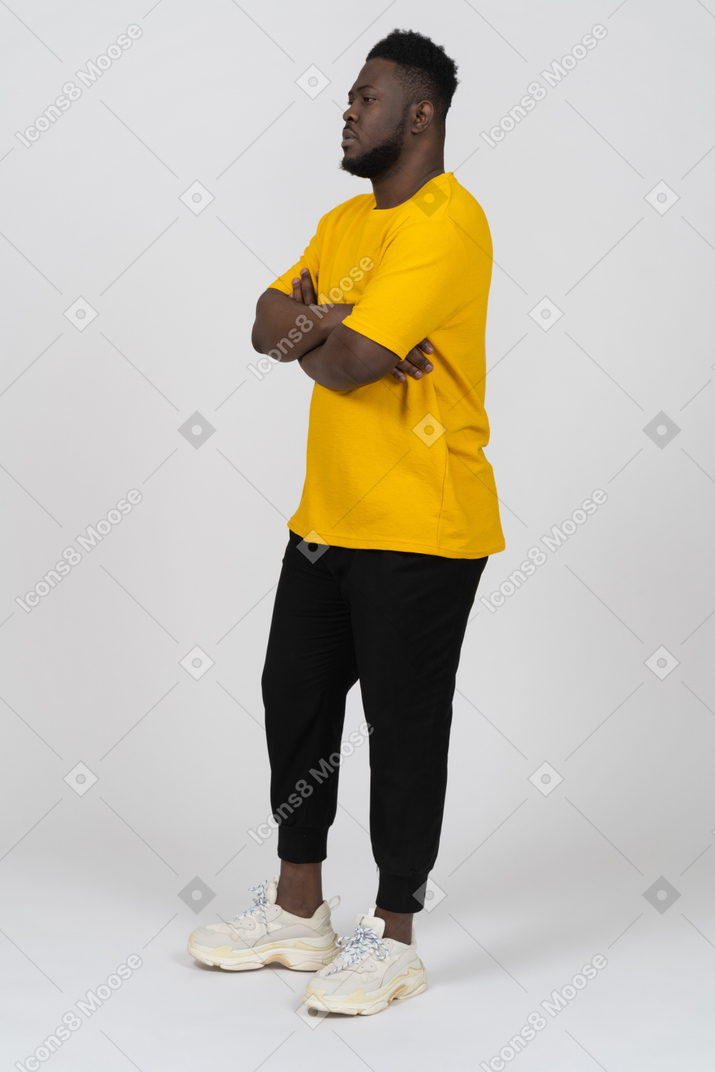一个身穿黄色 t 恤、双臂交叉的年轻深色皮肤男子的四分之三视图