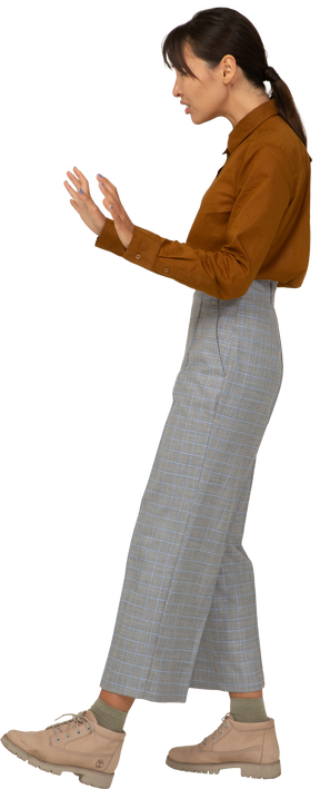 Vista lateral de uma jovem mulher asiática cuidadosa de calça e blusa, estendendo os braços