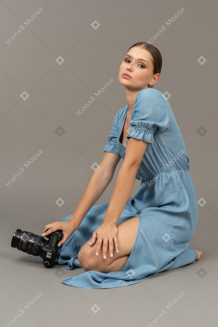 카메라와 함께 바닥에 앉아 파란 드레스에 젊은 여자의 측면보기