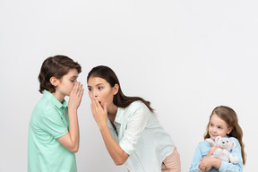 Junge flüstert in mamas ohr, während seine schwester plüschtier hält