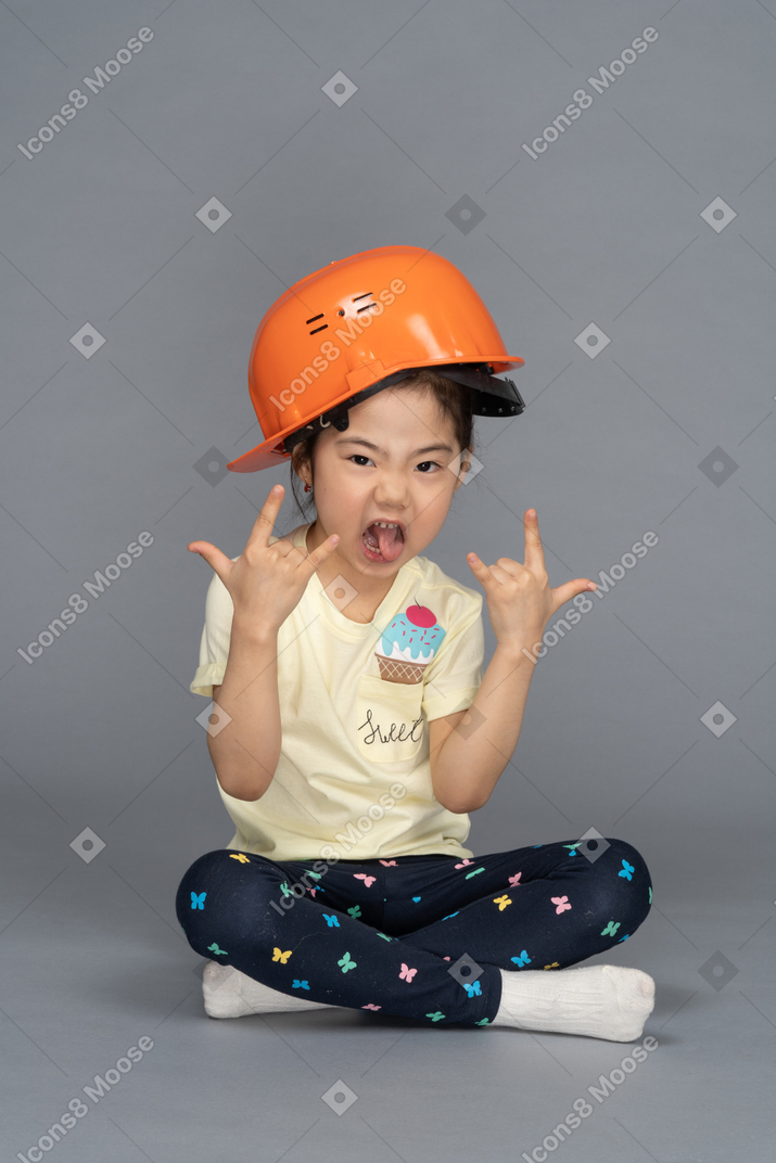 Retrato de uma menina fazendo sinais de pedra e enfiando a língua para fora