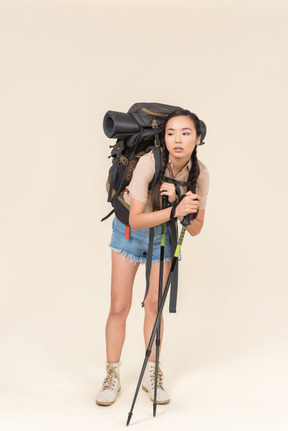 Tired young hiker woman standing with huge backpack and leaning on trekking poles