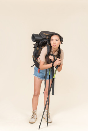 Femme jeune randonneur fatigué debout avec énorme sac à dos et s'appuyant sur des bâtons de trekking