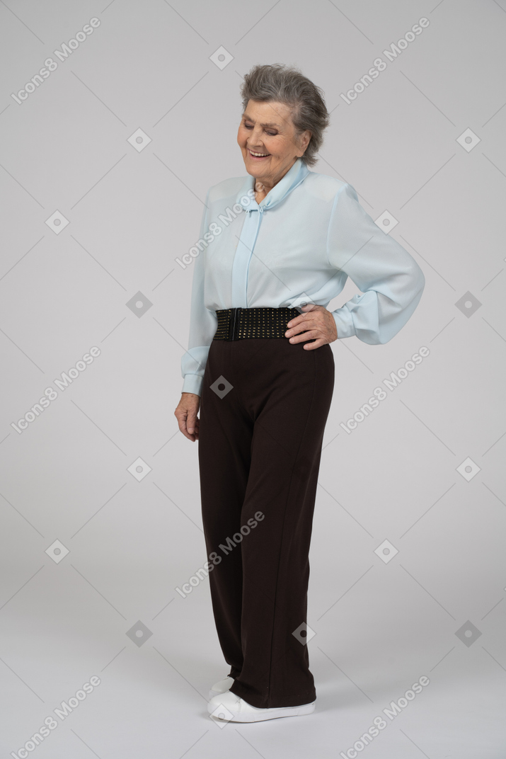 Three-quarter view of an old woman smiling with a hand on a hip