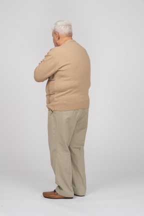 Side view of an old man in casual clothes standing with crossed arms