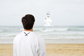 拉丁裔男子看着一个女人机器人站在海边，看着他