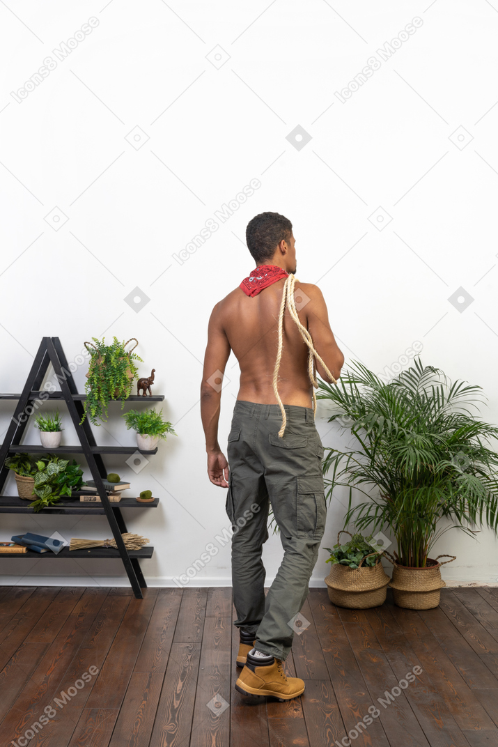 Muscular man with rope on his shoulder walking away from the camera