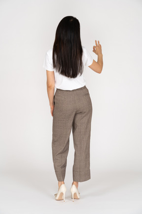 Vista posteriore di una giovane donna in calzoni che mostra segno ok