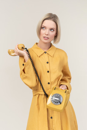 노란색 오래 된 로타리 전화를 들고 부주의 한 젊은 여자