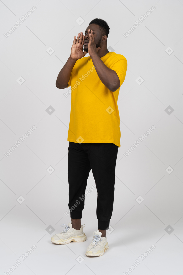 Vista de três quartos de um jovem de pele escura gritando em uma camiseta amarela