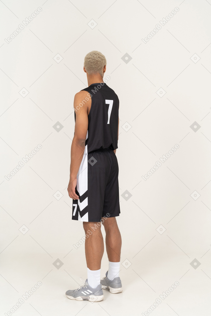 Vista posteriore di tre quarti di un giovane giocatore di basket maschile che guarda in alto