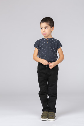 Vista frontal de un lindo niño chico en ropa casual mostrando la lengua y mirando a un lado