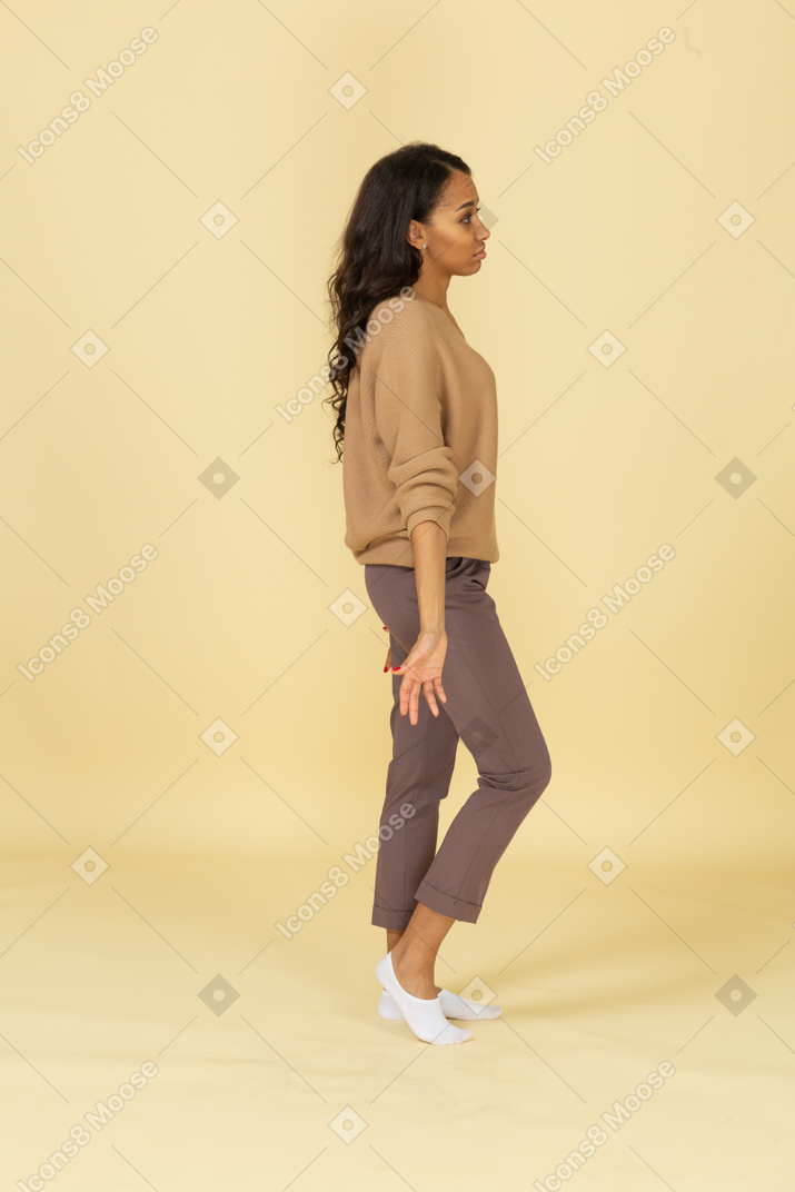 Vista lateral de una mujer joven descuidada de piel oscura extendiendo sus brazos