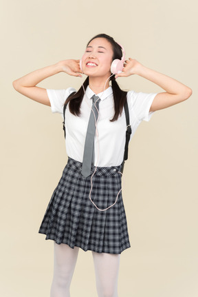 눈을 가진 아시아 학교 소녀는 헤드폰에서 음악을 듣고 폐쇄