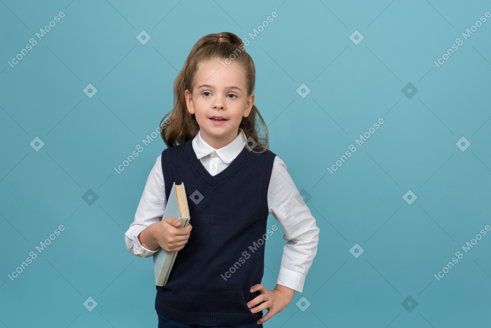 Маленькая школьница держит книгу и указывает на что-то