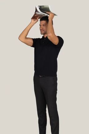 Standing in profile young man in black pants and t-shirt standing with magazine on his head