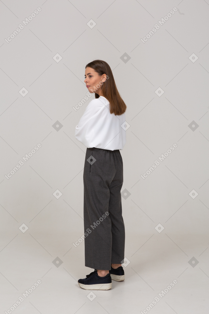 Three-quarter back view of a surprised young lady in office clothing crossing arms