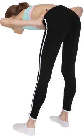 Vista posterior de tres cuartos de una jovencita en ropa deportiva poniendo las manos en las caderas mientras se inclina hacia adelante