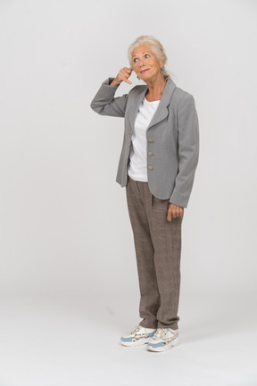 Vista laterale di una vecchia signora in abito che fa un gesto di telefonata