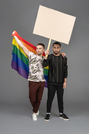 Vista frontal de dois jovens levantando um outdoor e bandeira lgbt