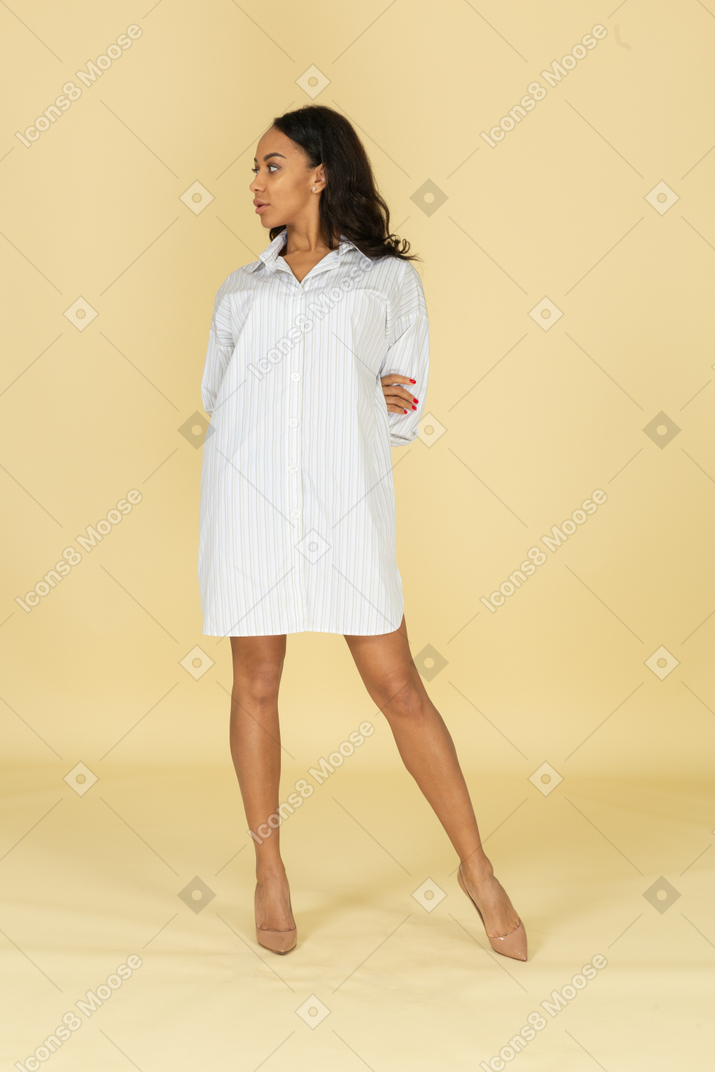 Vista frontal de uma jovem mulher de pele escura em um vestido branco de mãos dadas para trás