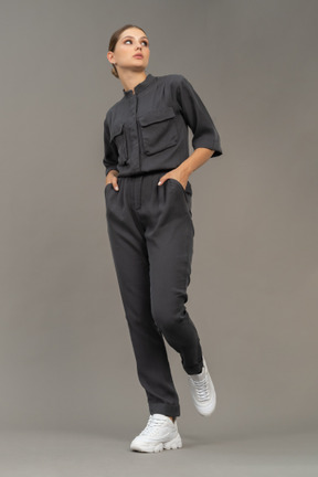 Front view of a walking young woman in a jumpsuit holding hands in pockets