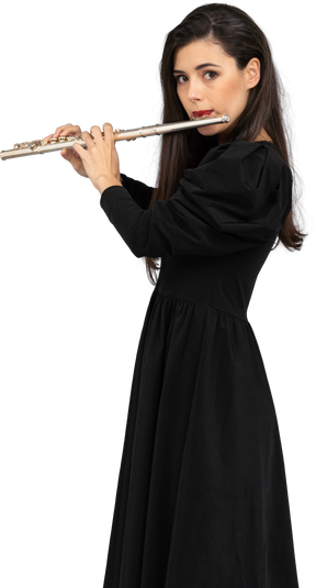 Вид сбоку серьезной молодой леди в черном платье, играющей на флейте