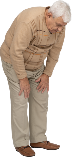 Side view of an old man in casual clothes bending down and touching his hurting knee