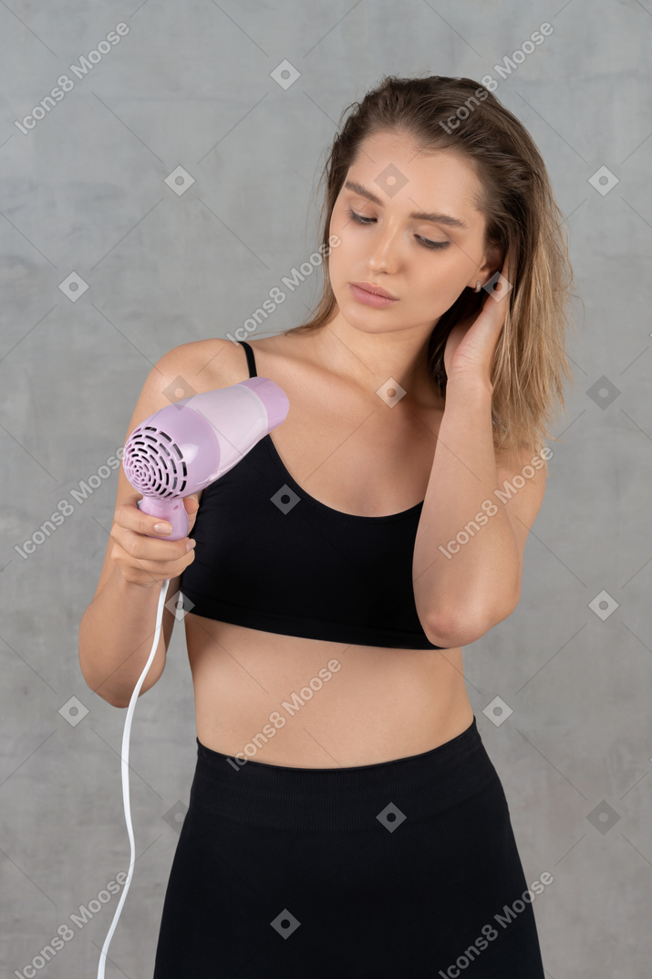 Front view of a young woman blow-drying her hair