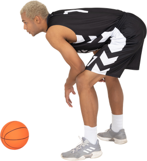 Vista laterale di un giovane giocatore di basket maschile in piedi vicino alla palla