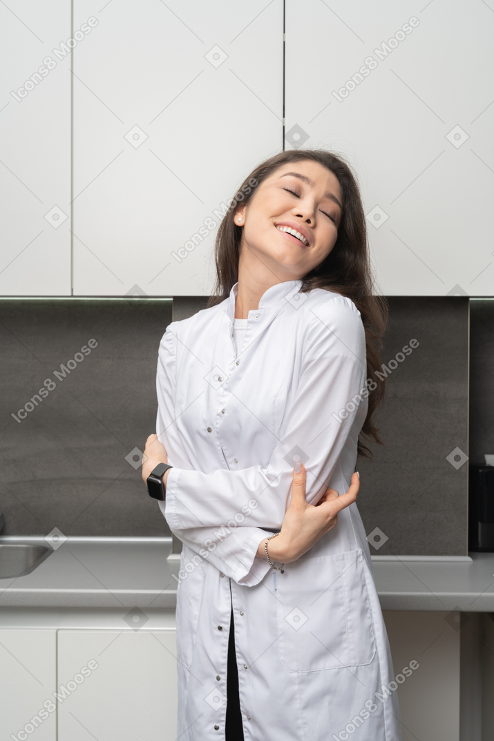 Three-quarter view of a pleased female  doctor hugging herself