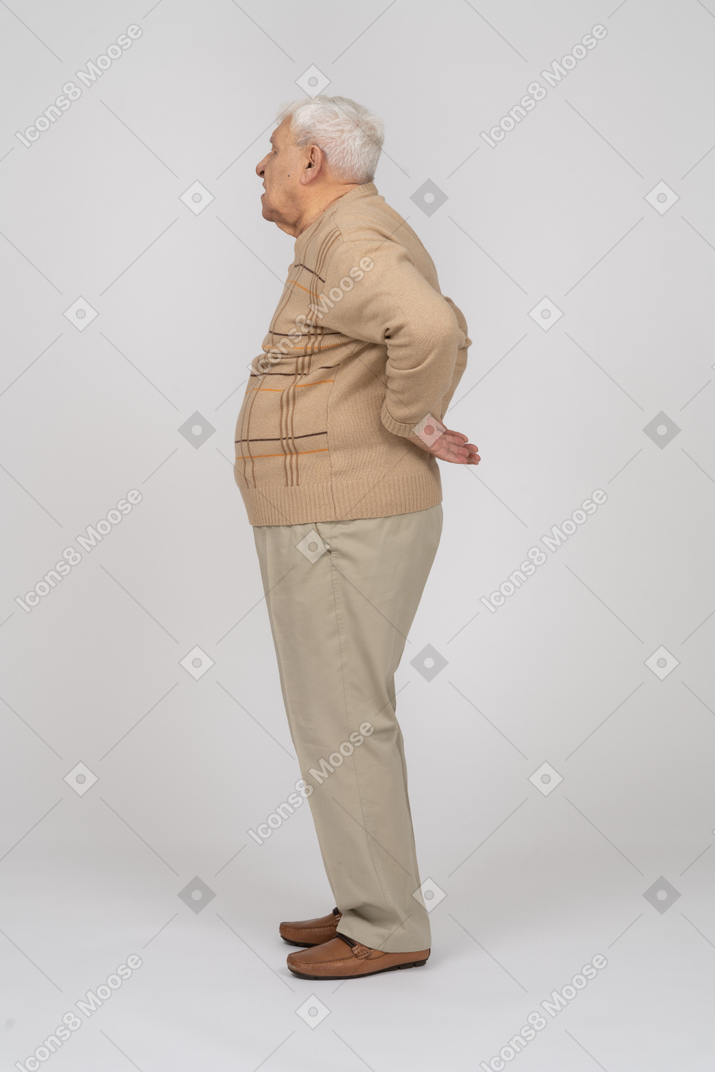 背中の痛みに苦しんでいるカジュアルな服を着た老人の側面図