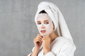 Woman in bathrobe using a sheet mask