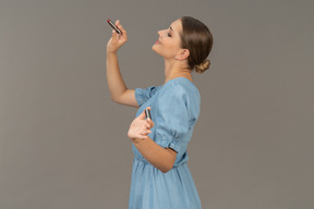 Вид сбоку молодой женщины в синем платье, держащей помаду