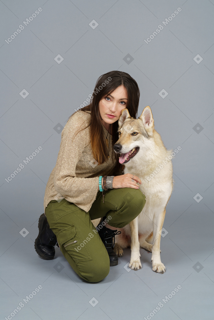 A figura intera di un maestro femmina seduto dal suo cane e guardando la fotocamera