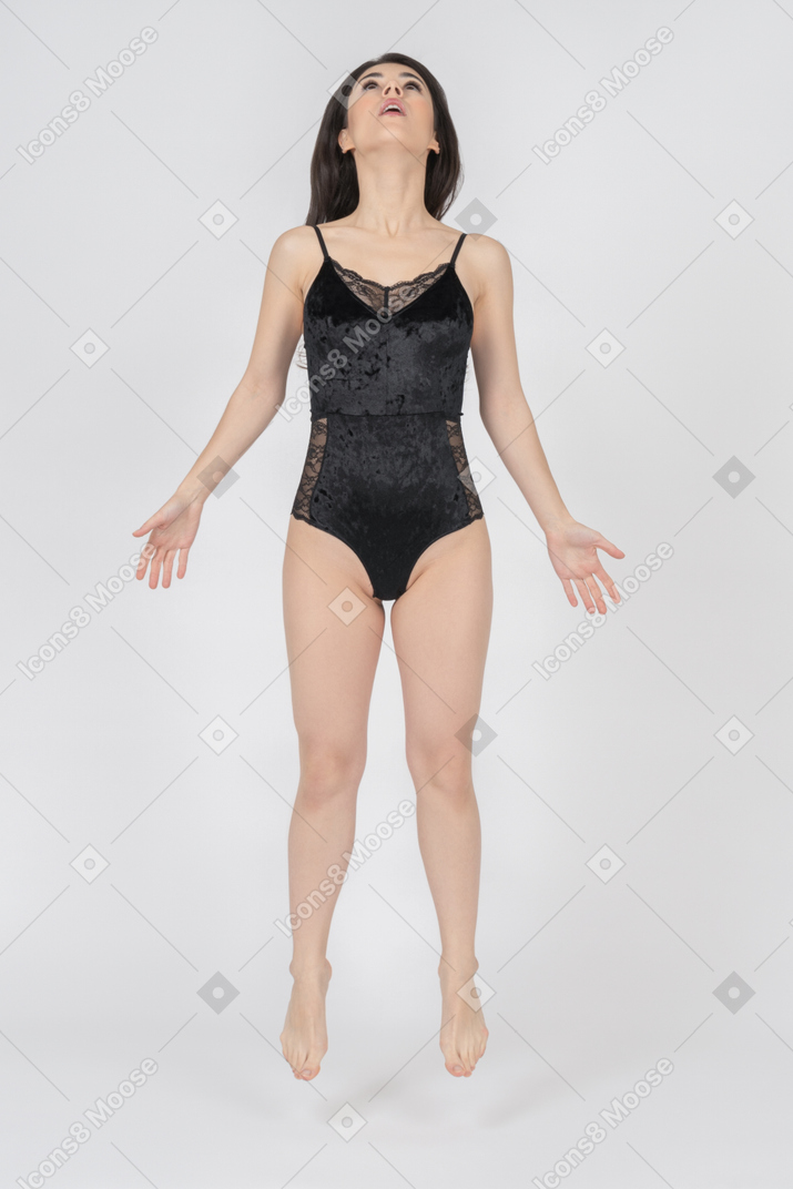 Young woman in black velvet bodysuit jumping with hands spread apart