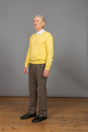 Vista de três quartos de um velho descontente vestindo um pulôver amarelo e olhando para cima