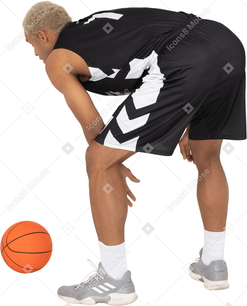 Three-quarter back view of a young male basketball player standing by the ball