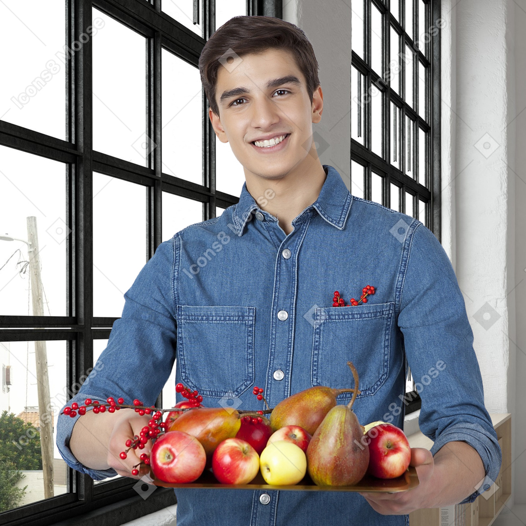 A man holding a tray of fruits in front of a window