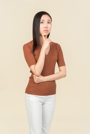 Задумчивая молодая азиатская женщина касаясь подбородку пальцем