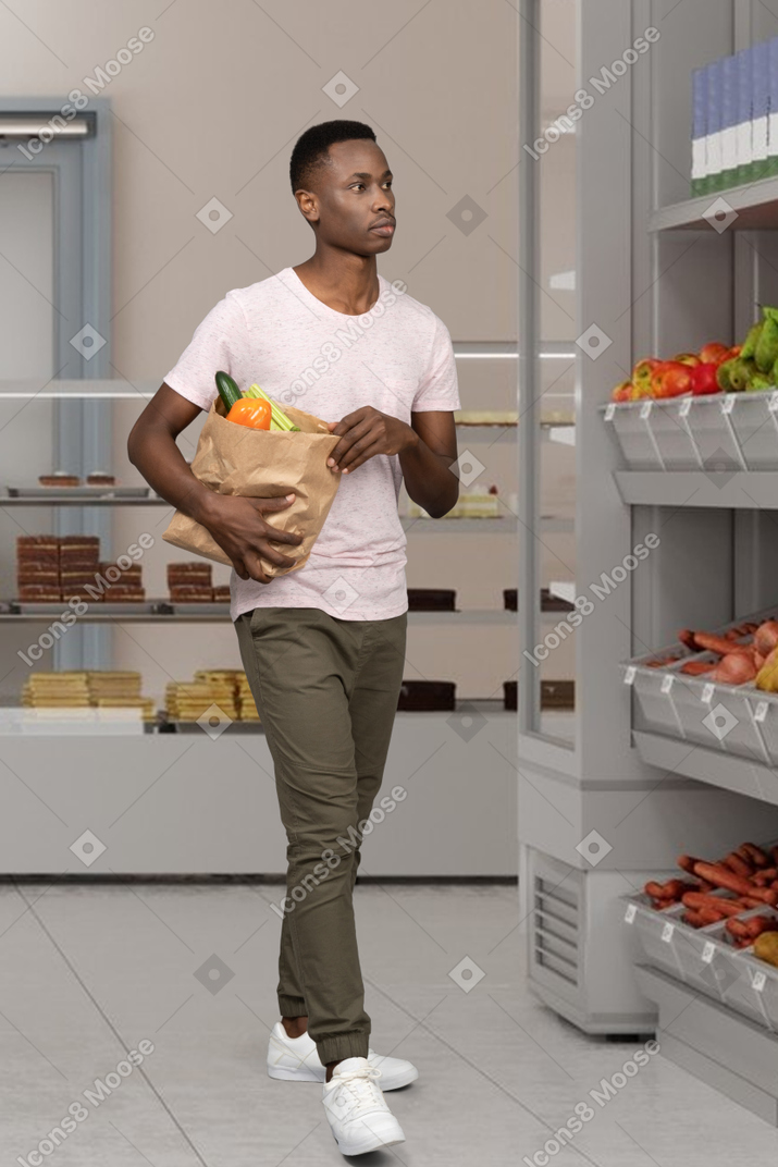 Uomo che cammina intorno a un supermercato con un sacchetto di generi alimentari