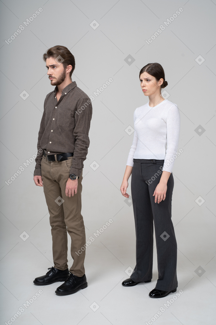 Three-quarter view of a young couple in office clothing standing still & knitting brows
