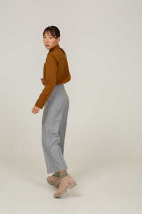 Three-quarter back view of a young asian female in breeches and blouse turning away