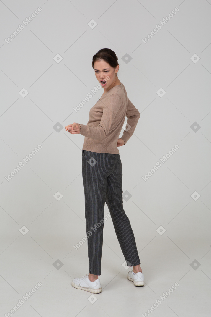 Three-quarter back view of a furious young lady in beige pullover pointing finger