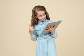 Mignonne petite fille tenant une tablette et montrant les pouces vers le haut