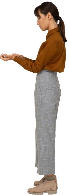 Вид сбоку молодой азиатской женщины в бриджах и блузке, застегивающей манжеты