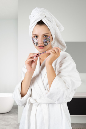 A woman with eye patches in bathrobe holding a nail file