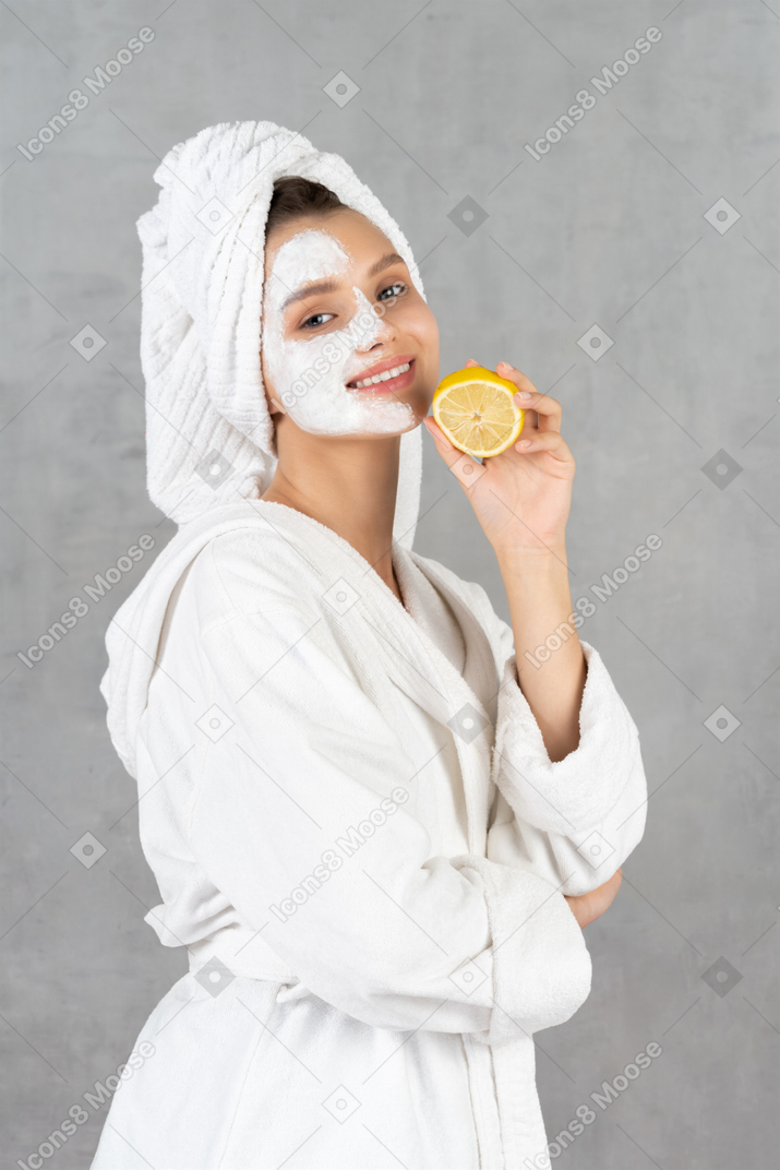 Mujer joven sonriente en bata de baño con un limón en la mano